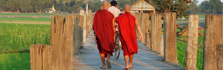 Viaggio Birmania monaci con tonache rosse percorrono il ponte in tek ad Amarapura